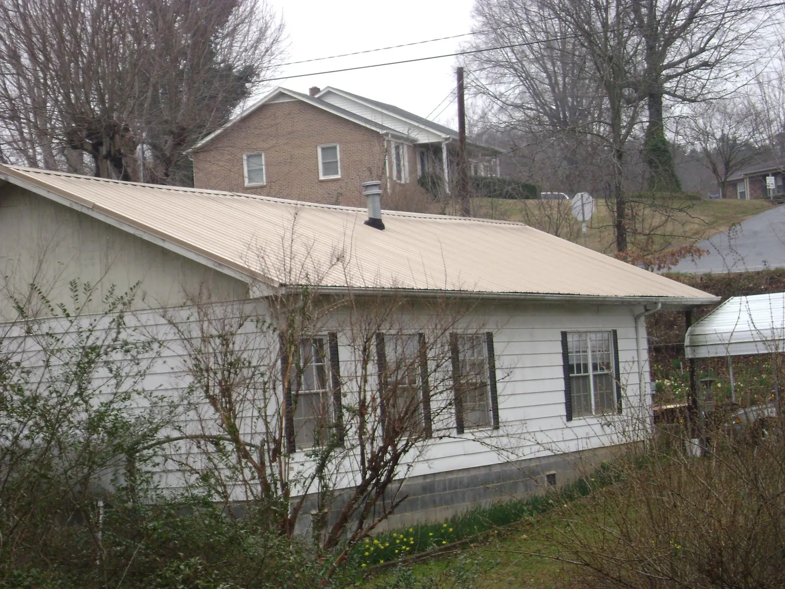 Tan metal roof on a white sided house set into a hillside — Commercial Roofing by Roofing Brothers in Cedarville